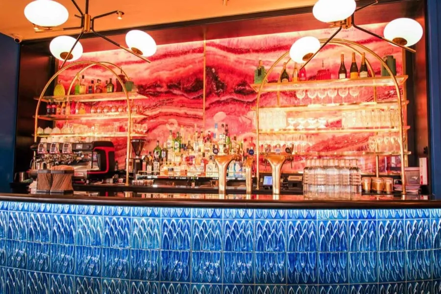 The bar at Les Pipelettes du Boulevard, blue tiled counter and pink marble mural